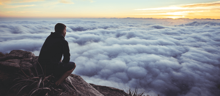 Person overlooking clouds from mountain peak